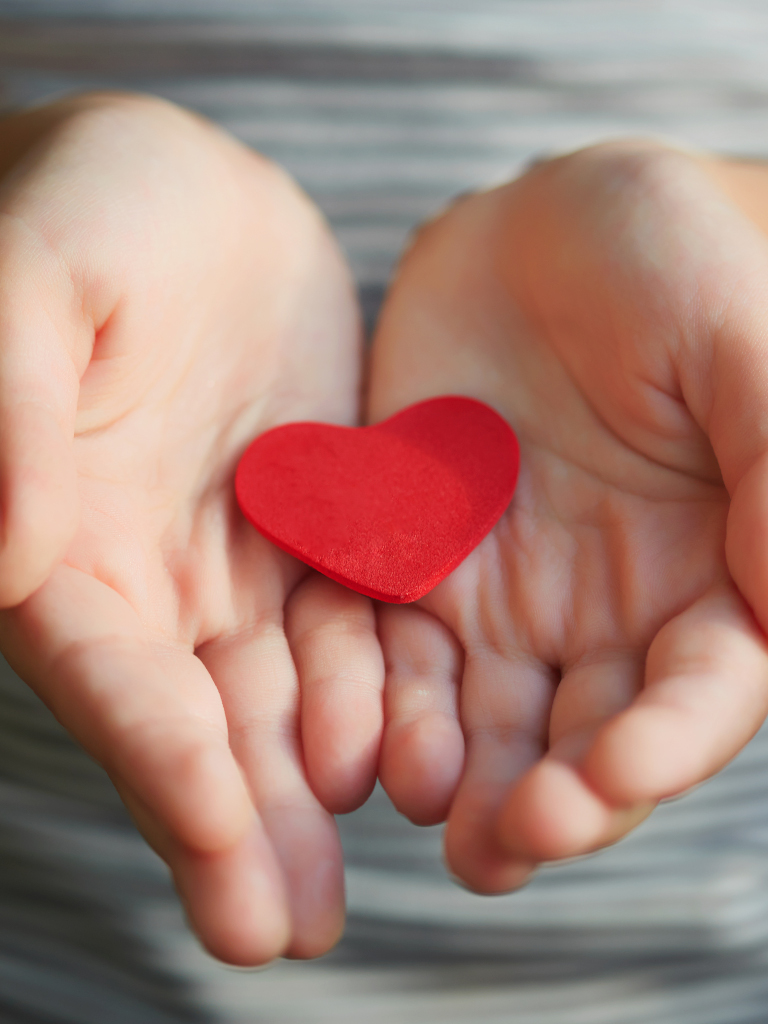 Ein Kind hält behutsam ein rotes Herz aus Filz in den Händen und heisst Sie herzlich willkommen