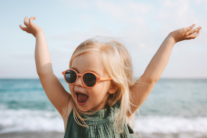 Kleines Maedchen mit Sonnenbrille freut sich, dass die reisebegeisterte Babysitterin aus Salzburg auch am Strand mit dabei ist