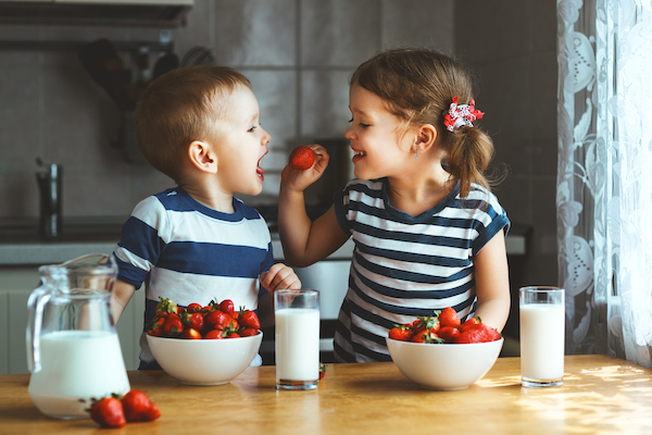 Zwei Kinder essen gemeinsam Erdbeeren während der Nachmittagsjause mit der Nanny