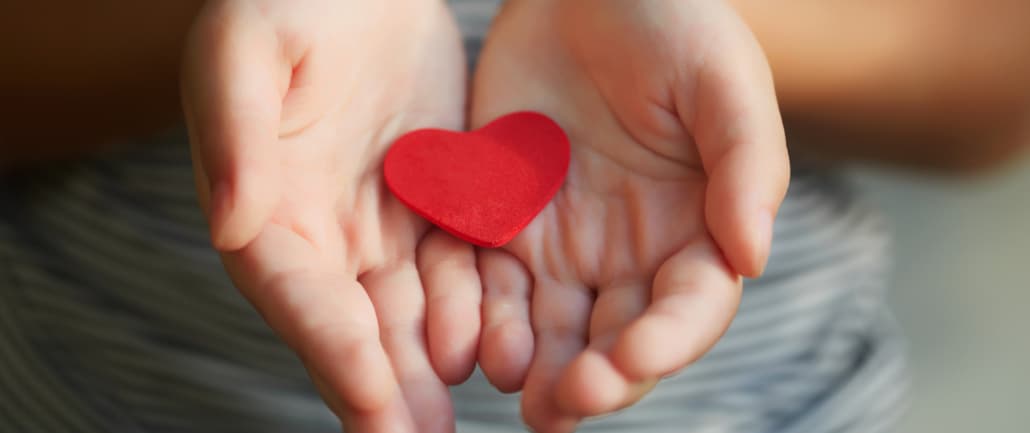 Ein Kind hält behutsam ein rotes Herz aus Filz in den Händen und heisst Sie herzlich willkommen